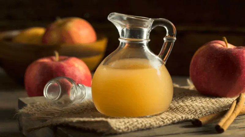 Glazen kan met appelazijn en appels op tafel