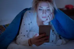 Jonge vrouw ligt in bed en kijkt op haar smartphone