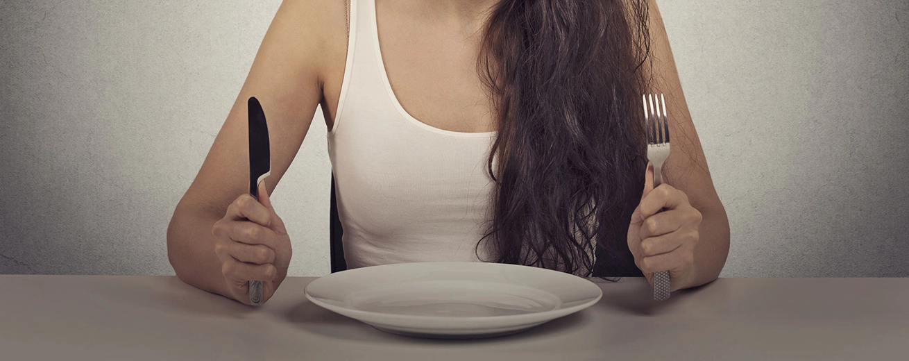 Vrouw zit aan tafel en is moe van dieetbeperkingen met leeg eetbord met vork en mes