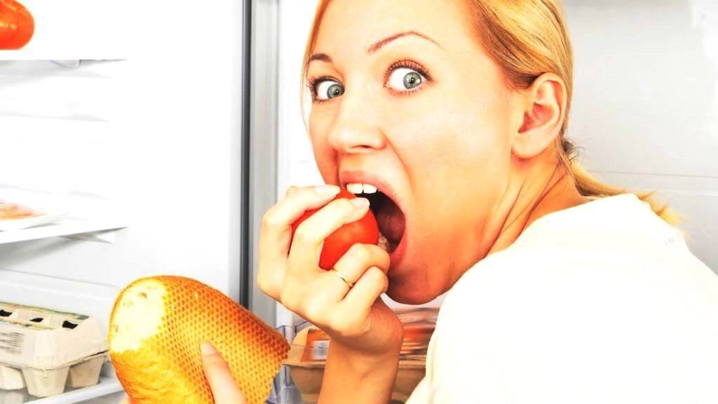 photo d'une femme mangeant devant un réfrigérateur ouvert