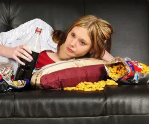 Vrouw ligt op de bank met cola en chips
