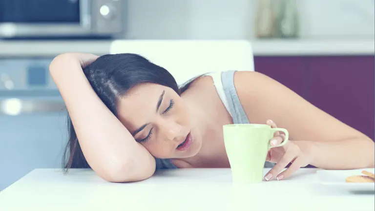 Vrouw ligt op tafel te slapen met een kopje koffie ernaast