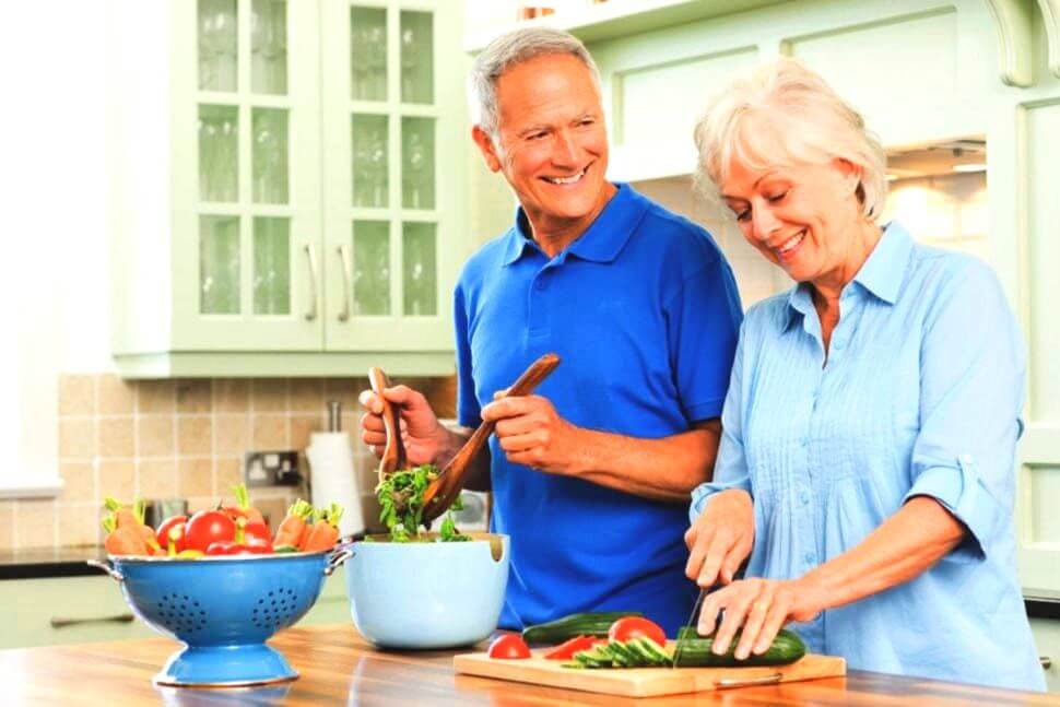 Ouder echtpaar snijdt samen groenten in de keuken