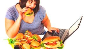 Vrouw met overgewicht eet vanachter de laptop