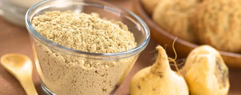 poedervormige maca of peruaanse ginseng in een glazen kom met melk, chocoladedrank, maca-koekjes en maca-wortels