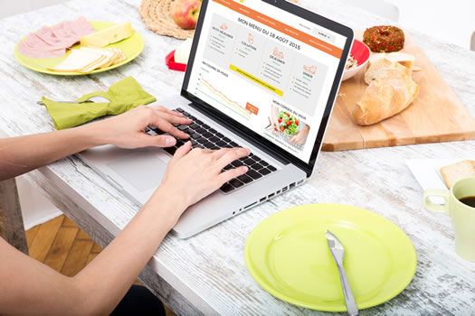 Vrouw bekijkt via laptop de Croq'kilos dieet website met op tafel gezonde voedingsproducten 