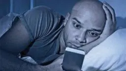 man ligt in bed en is gefocust op zijn smartphone