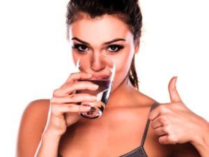 Vrouw drinkt glas water en houdt duimpje omhoog
