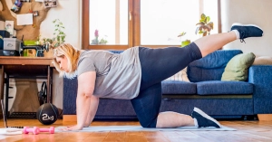 vrouw met overgewicht maakt sportbewegingen op yogamat in huiskamer