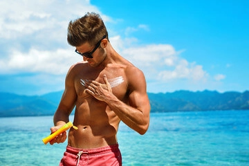 Gespierde man op het strand smeert zichzelf in met zonnebrandcrème 